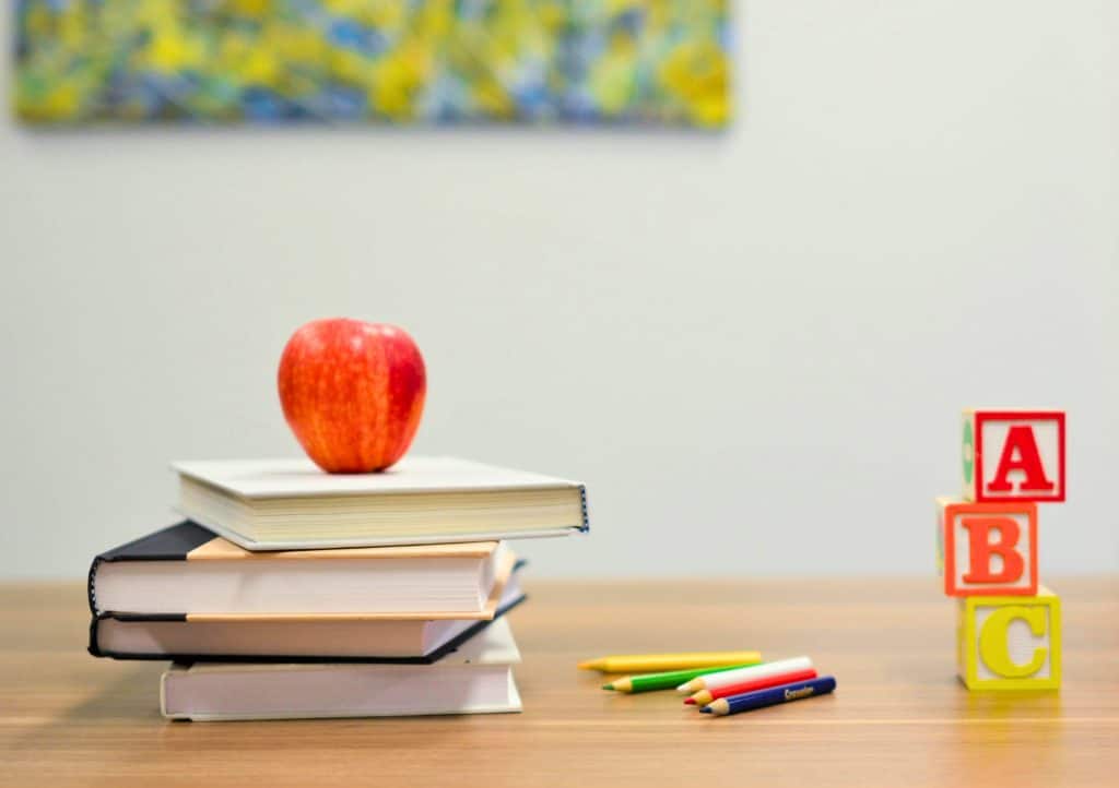 Red apple sitting on a stack of books, with various colored pencils and ABC blocks nearby.