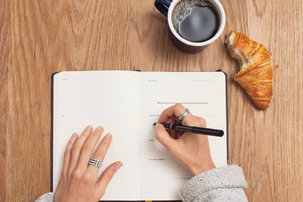 Wooden table set with an open journal, coffee cup, and a croissant. 