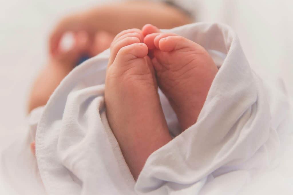 Newborn baby feet wrapped in a white swaddle blanket.
