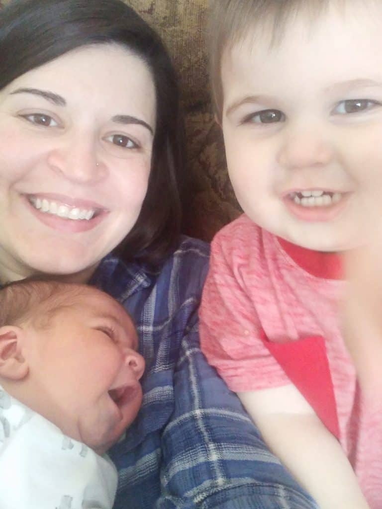 Mother smiling while cuddling a newborn and toddler.