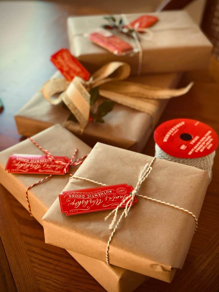 Four holiday gifts wrapped in brown paper and tied with red and white twine.