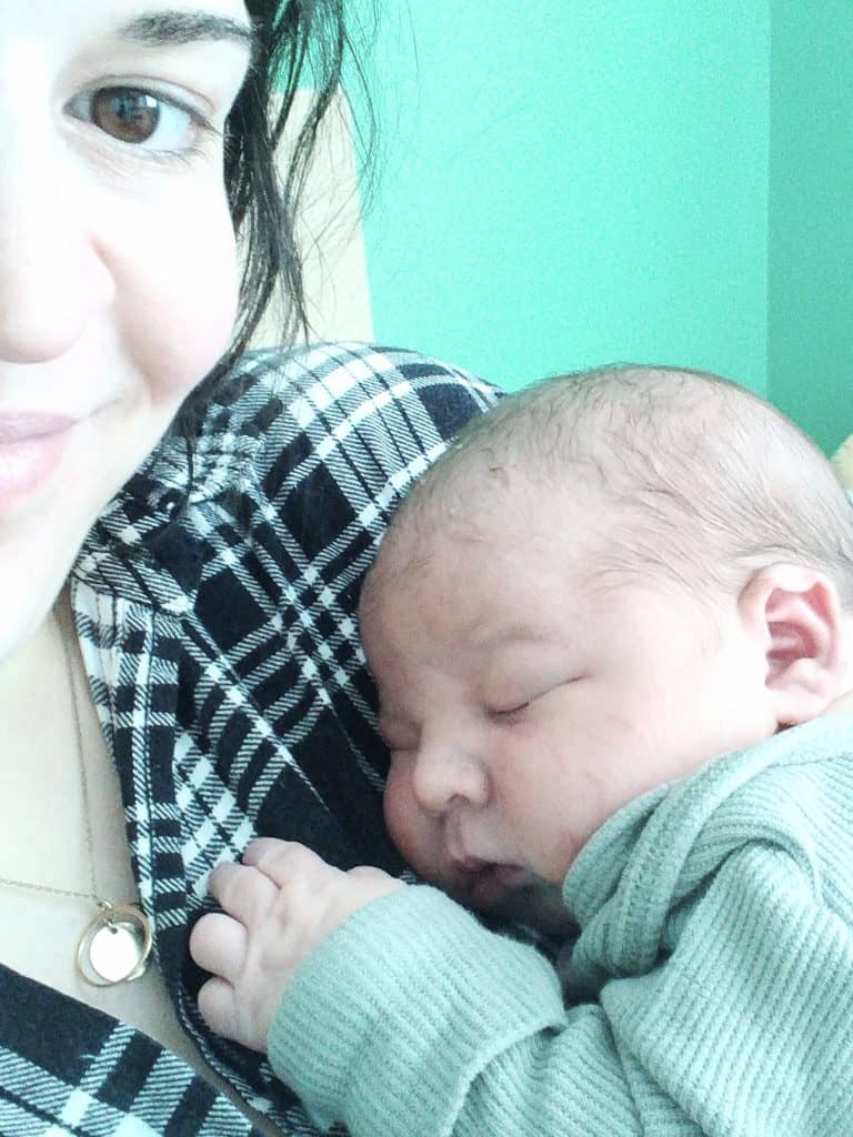 Up close of a mother smiling while holding her sleeping newborn baby boy wearing a green onesie.