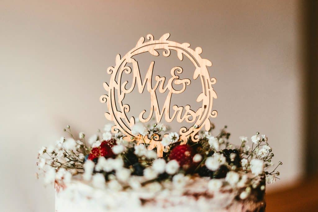 Mr. & Mrs. wooden cake topper on a white wedding cake with baby's breath and strawberries on top.