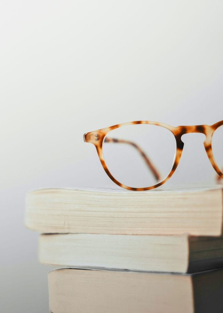 Stack of books with brown glasses resting on top.