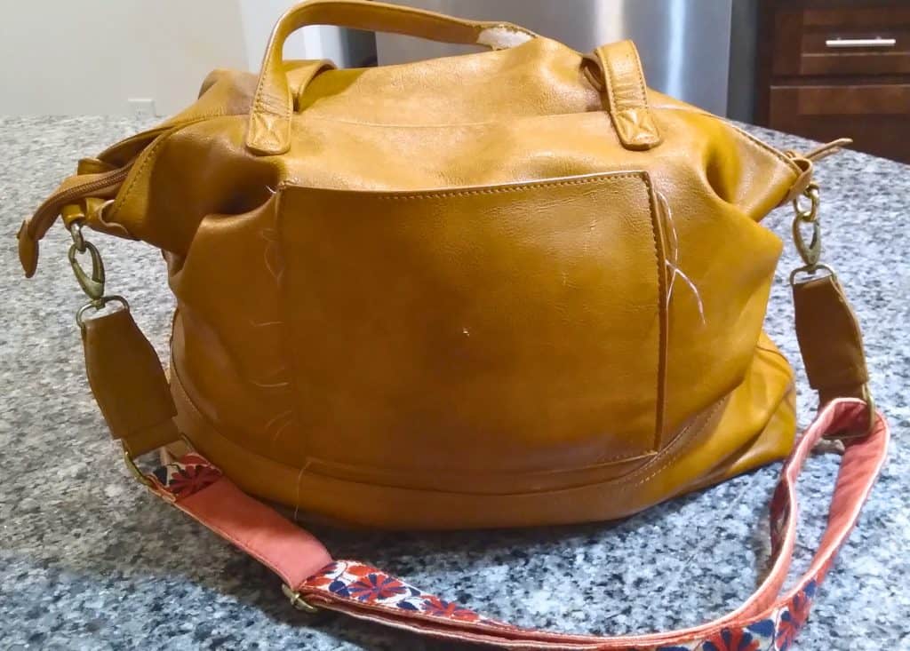 Bella Tunno Boss Bag Tote in the color Cognac with a red floral strap sitting on a marble counter.