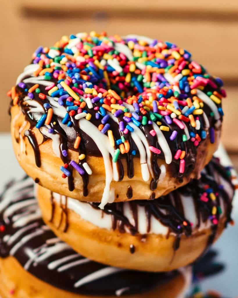 Up close picture of a stack of three assorted donuts covered in chocolate or vanilla icing and sprinkles.