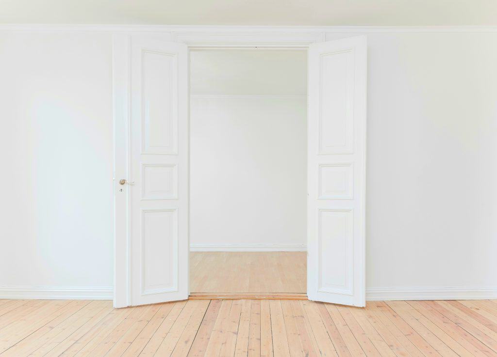 White walls, and white doors open to an empty room with wooden floors.
