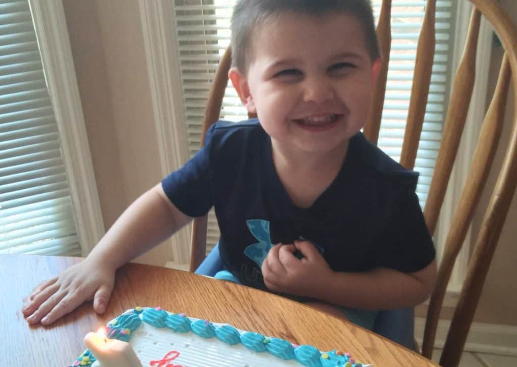 Young boy smiling before blowing out the candles on his cake with white and blue icing.