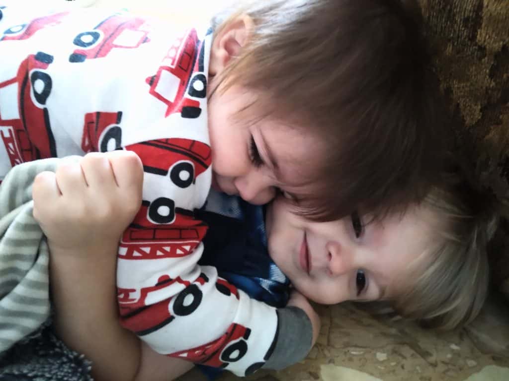Two toddler boys wearing firetruck pjs laying on the floor hugging.