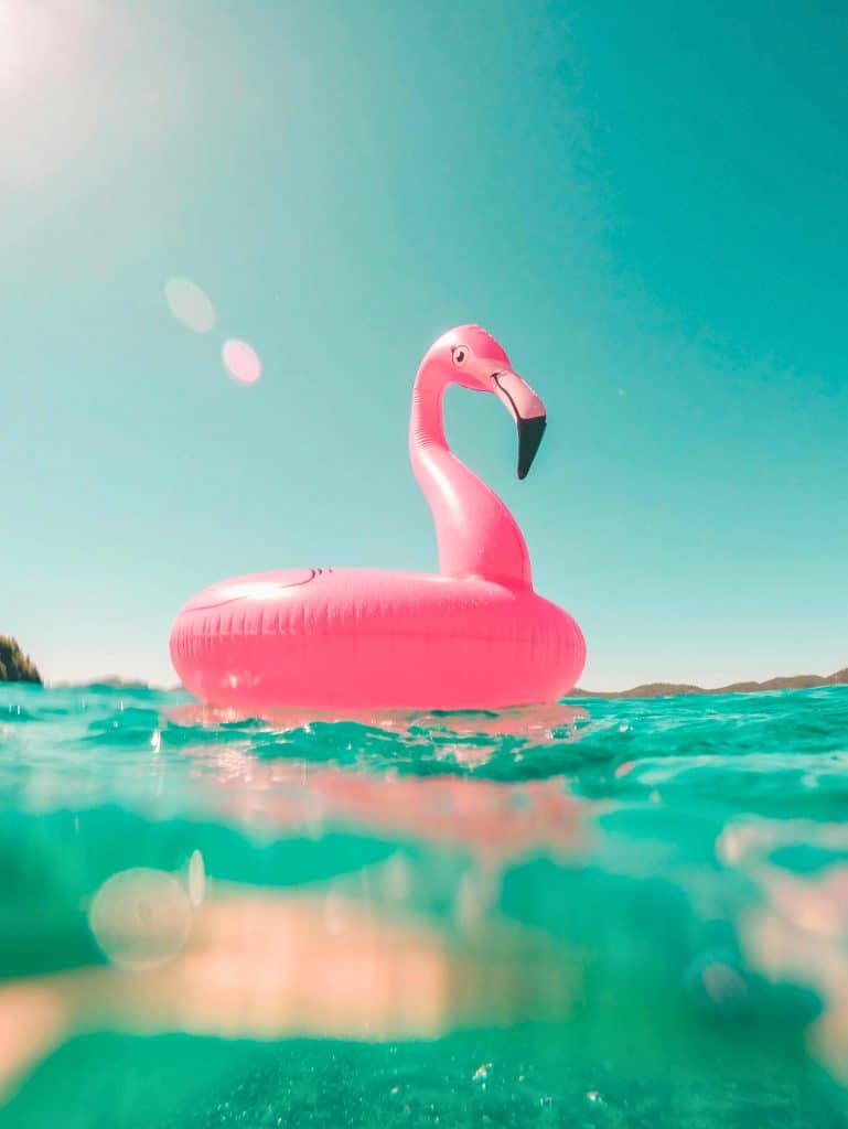 Giant pink flamingo floaty in a blue ocean under a bright cloudless blue sky.