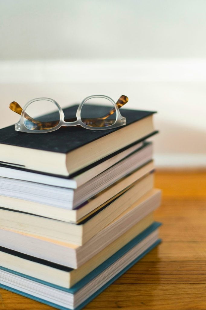 Stack of eight books with a pair of round glasses sitting on top.