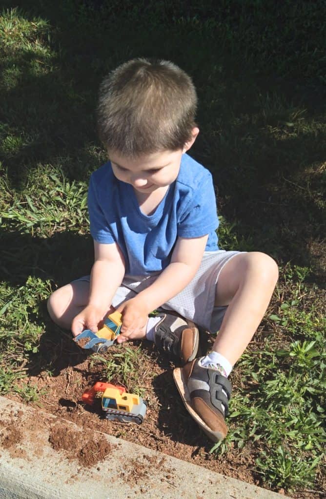 Young brown-haired boy with blue t-shirt and khaki shorts playing with construction toys in the dirt.