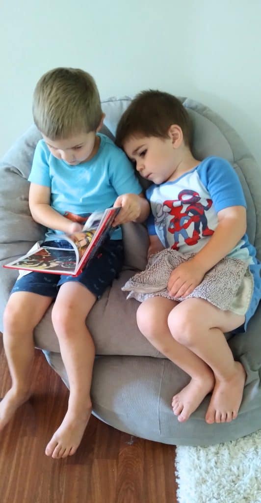 Two young boys cuddled on a beanbag reading a book together.