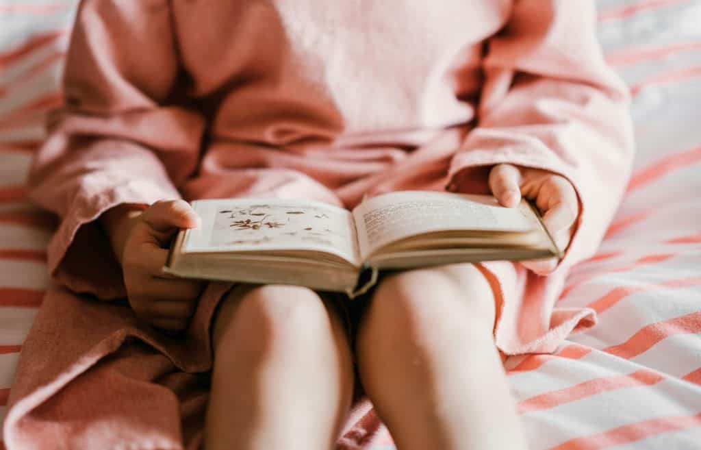 Young girl dressed in pale pink reading a chapter book.