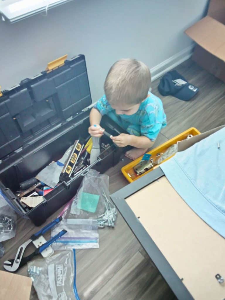 Young boy in a blue shirt playing in Dad's toolbox.