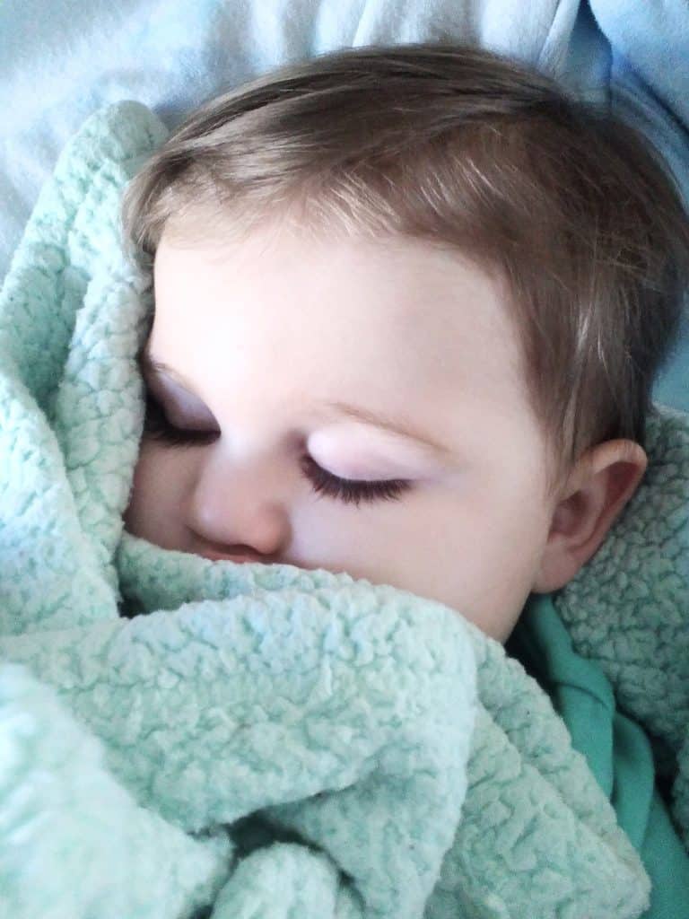 Toddler Boy asleep wrapped in a light green blanket.