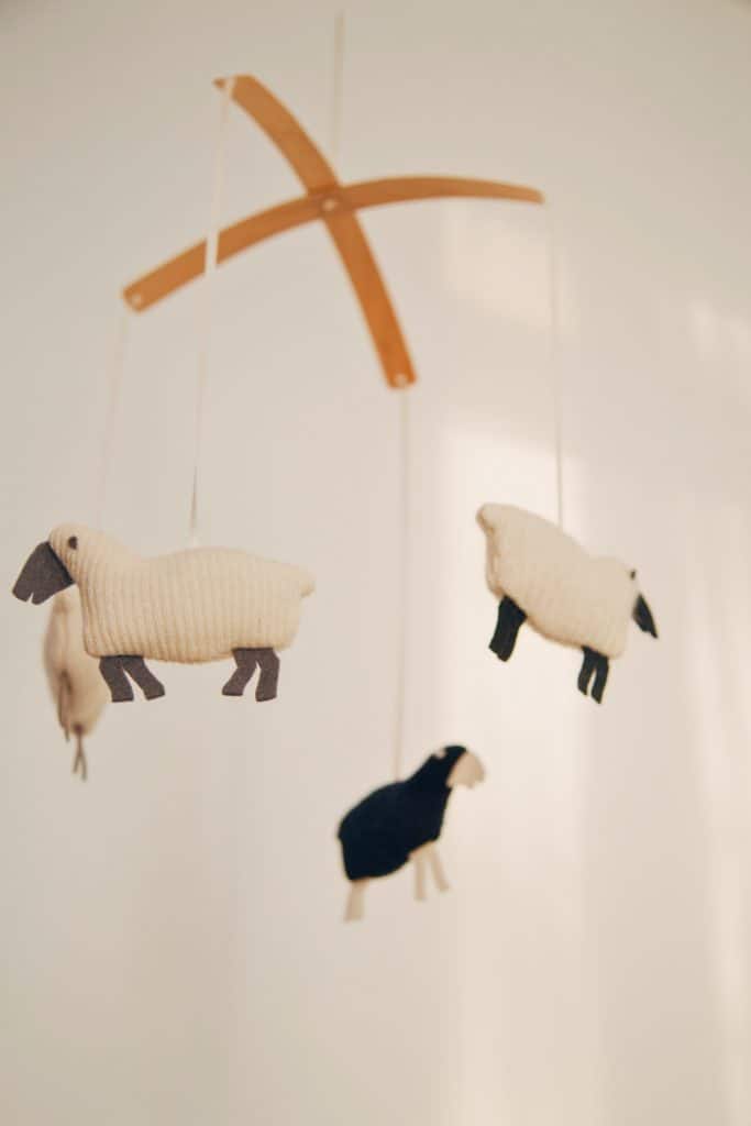 Wooden baby mobile with one black and three white wool sheep.