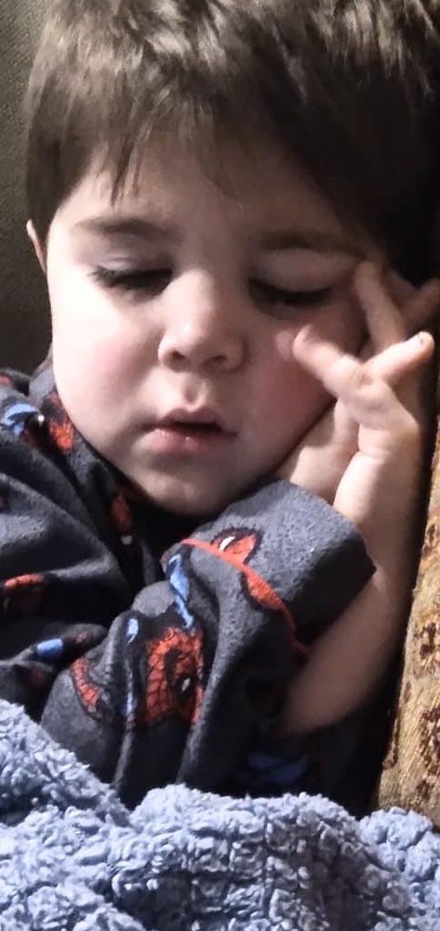 Toddler boy sleeping with his hands folded by his face and wearing Spiderman pajamas.